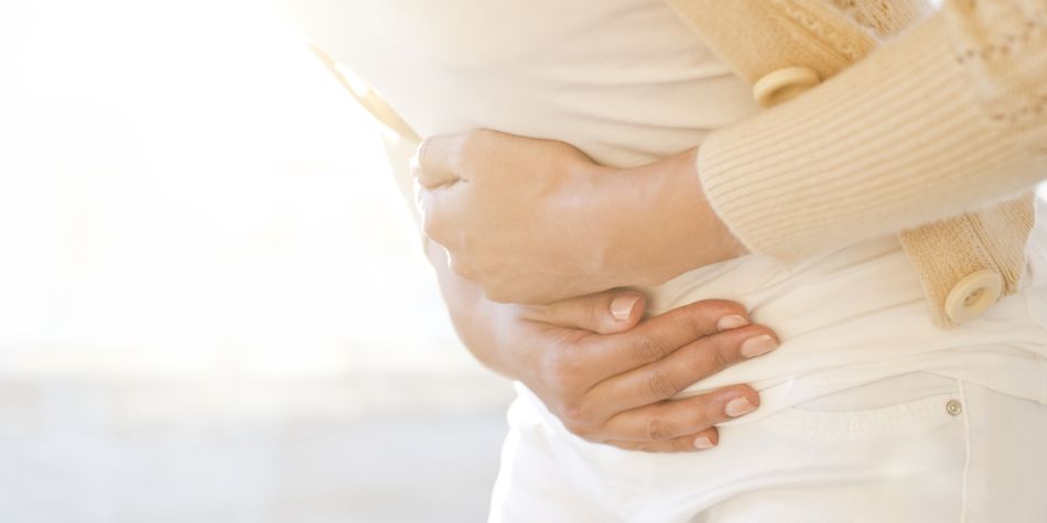 A woman wearing a knit sweater bends at the waist, holding her stomach.