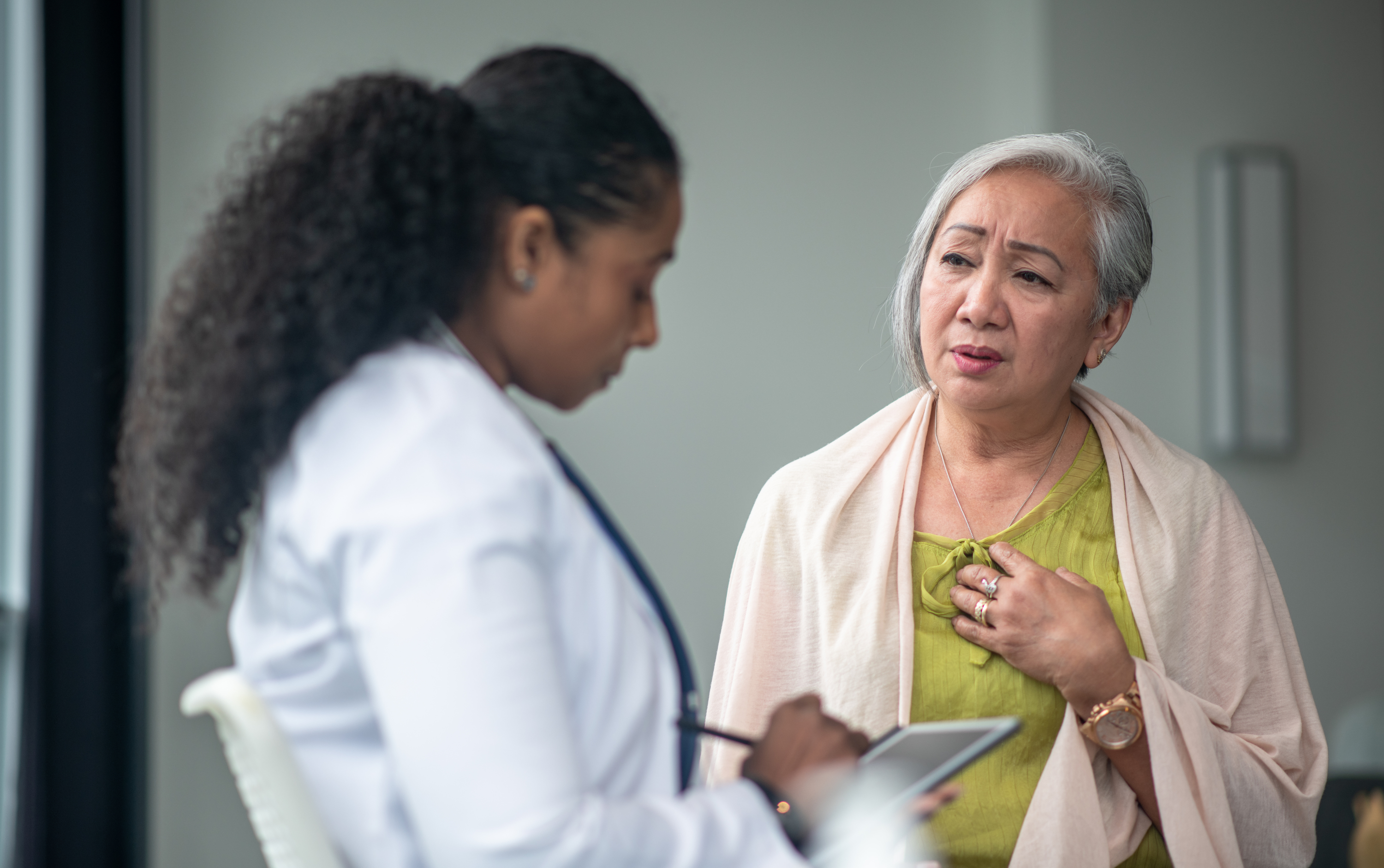 A woman talks with a healthcare provider while holding her chest during a medical visit.