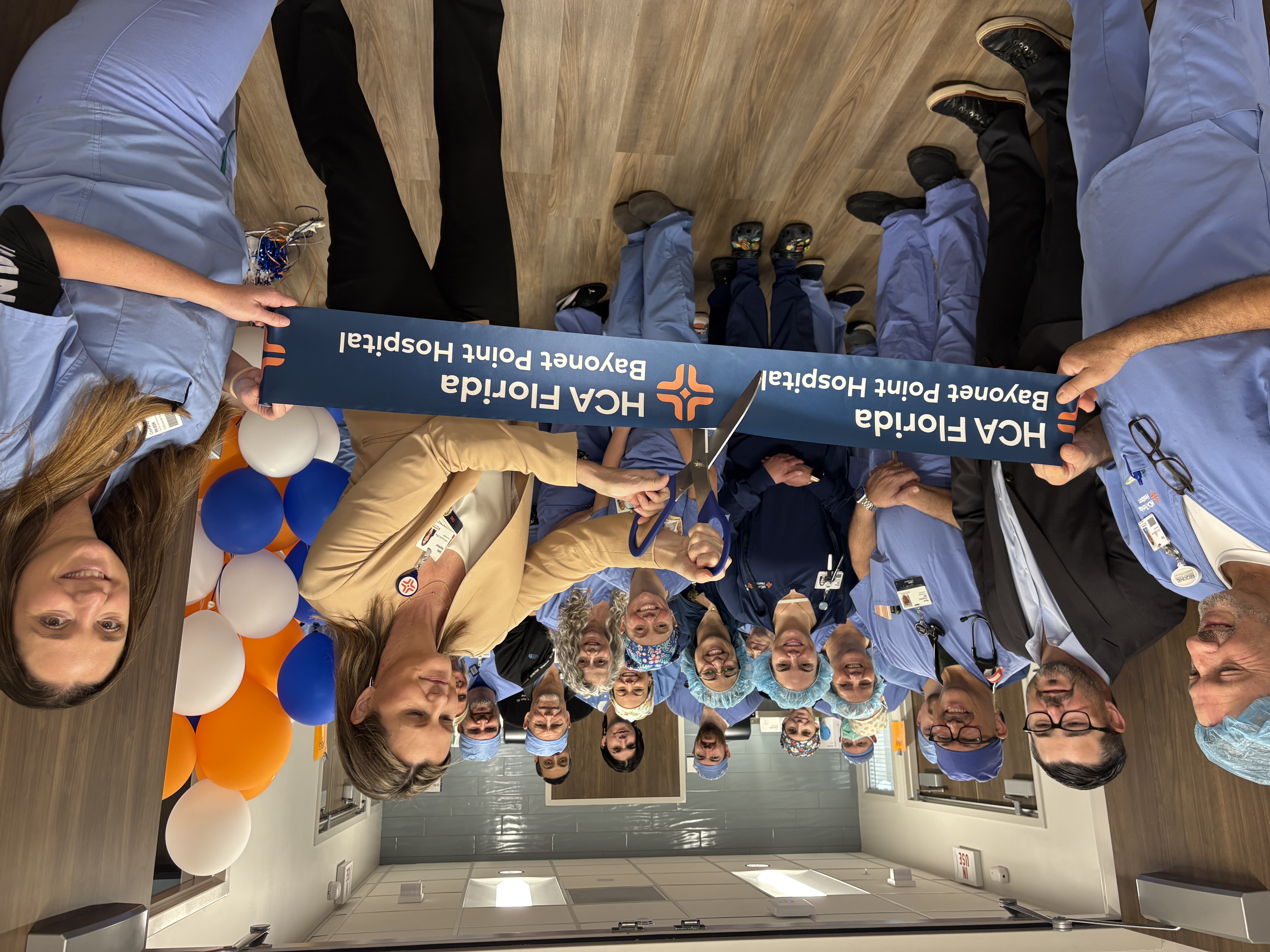 A group of HCA employees gather in a hospital hallway for a ribbon cutting ceremony.