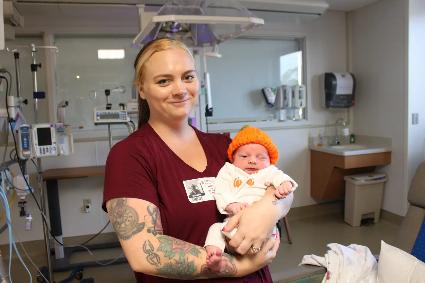 Oliver Lick, wearing a bright orange beanie, being held by a NICU nurse.