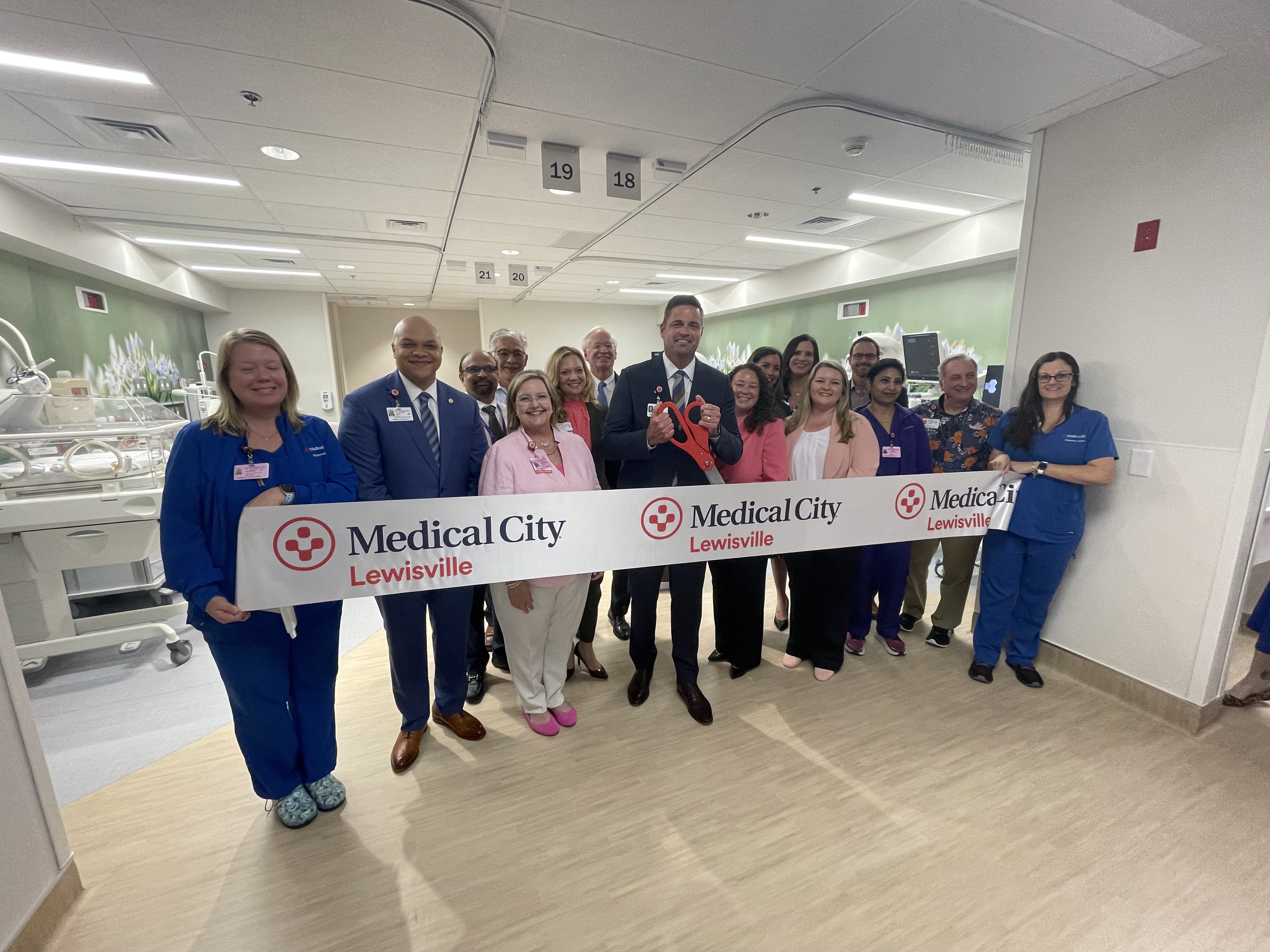 A group of people standing behind a large ribbon with the Medical City Lewisville logo repeated on it.