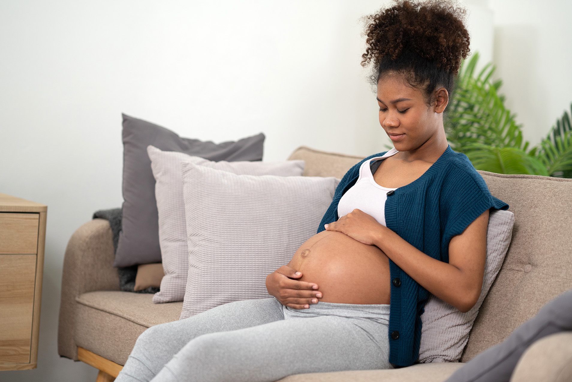 Pregnant woman sitting with baby in womb gently touching belly