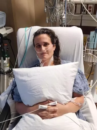 Angelica in the hospital holding a pillow in bed.