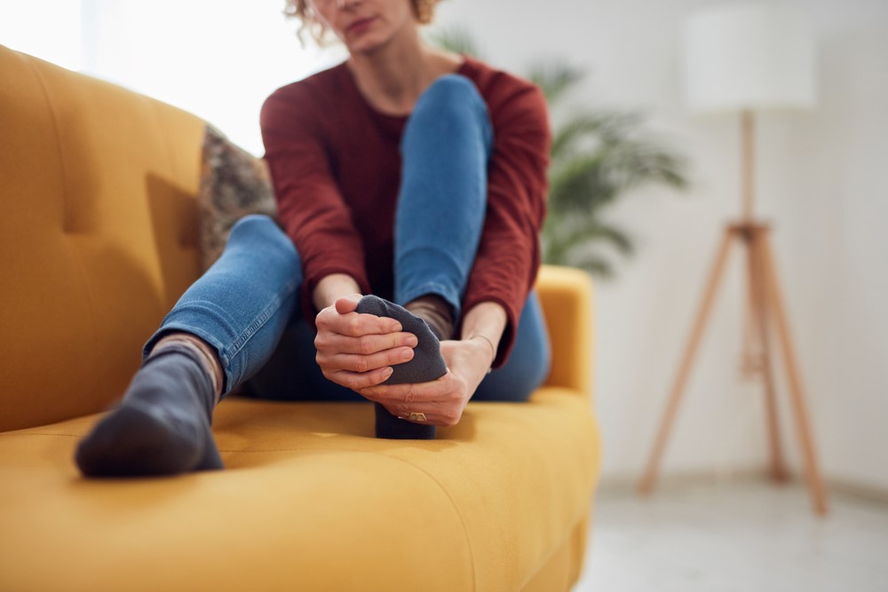 A woman rubs her foot while seated on a sofa in a living room.
