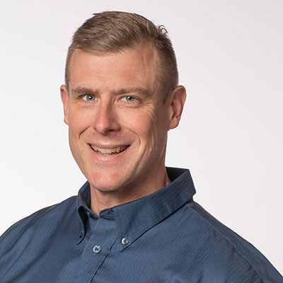 Mike Malay smiles while wearing a grey button-up shirt.