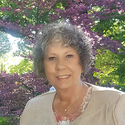 Jana Petersen smiles while standing outside in front of a flowering tree.