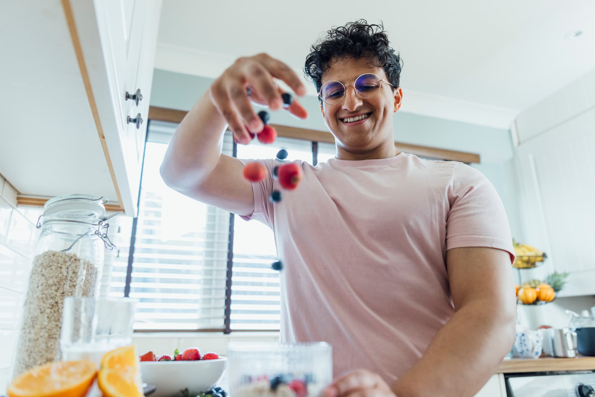 Young adult dropping fresh blueberries and strawberries into a plastic bowl.