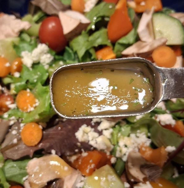 A serving spoon with homemade honey dijon mustard and tarragon dressing, with a fresh salad in the background.