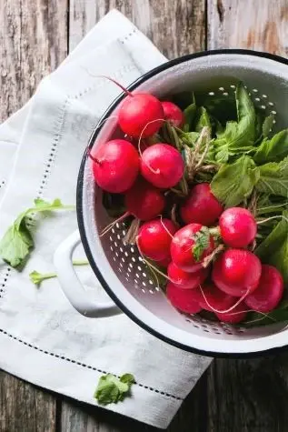 a white bowl of red radishes on top of a napkin on a wooden table