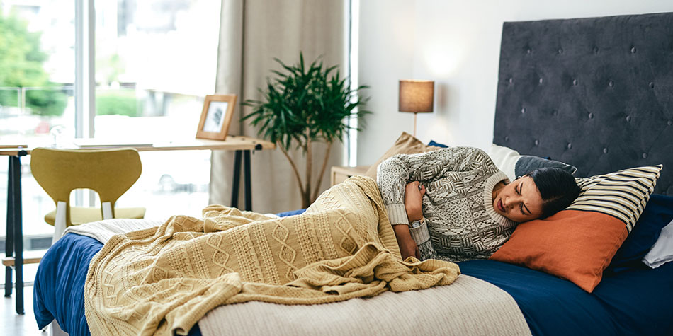 A woman lying in bed clutches her abdomen in discomfort.