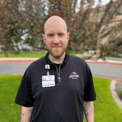 Surgery survivor David Riker wears a beard and hospital volunteer scrubs outdoors.