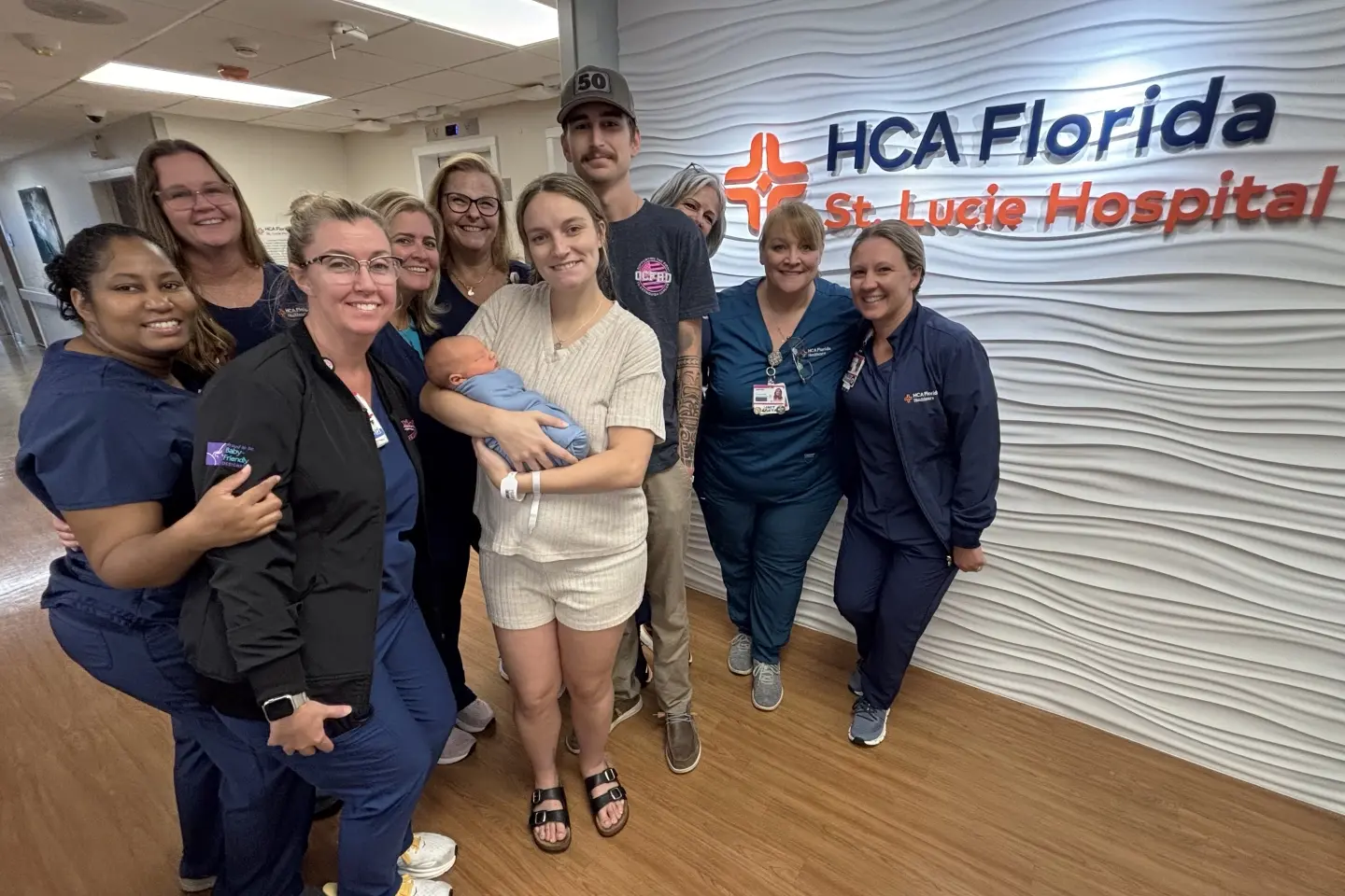 Olivia, Toby, their baby and the St. Lucie team posing by the hospital logo