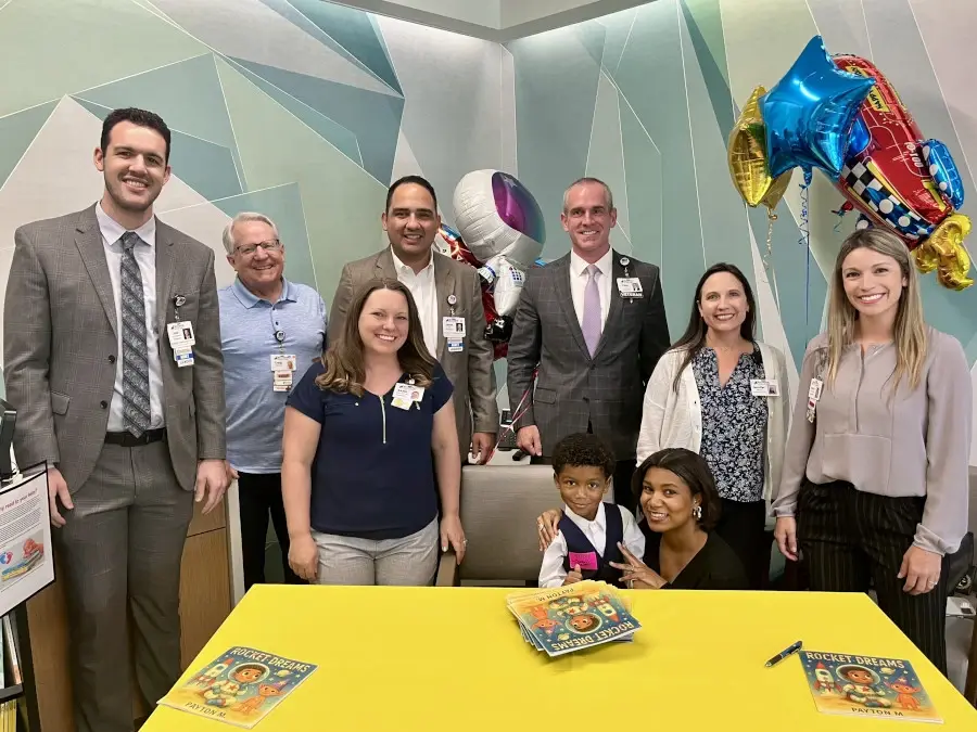 Male and female hospital staff surround young boy Payton seated at a table with books.