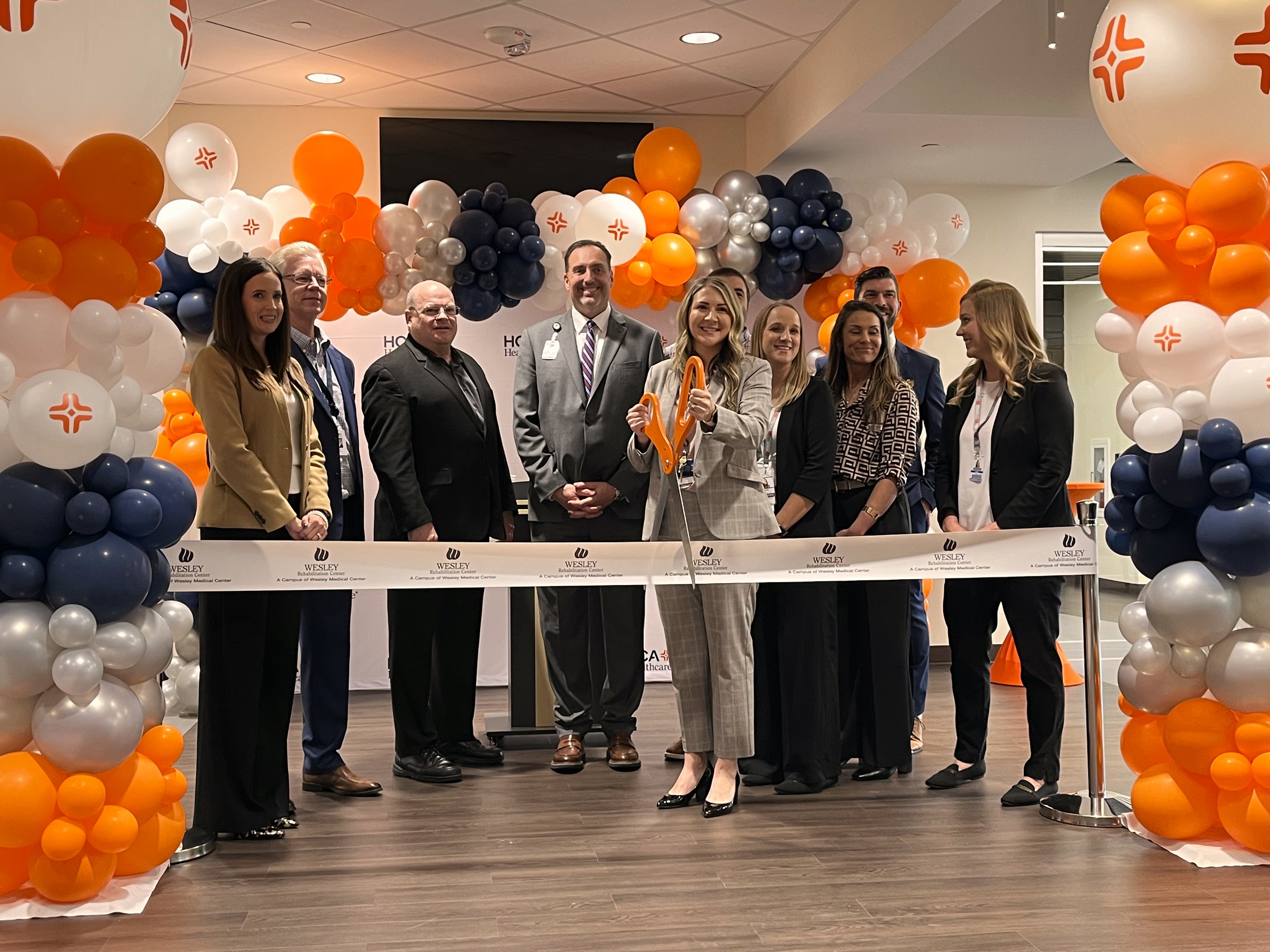 Wesley Healthcare team posing with ribbon and giant scissors for ribbon cutting