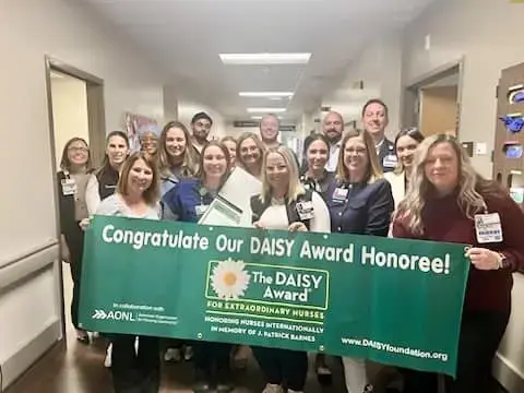 Colleagues hold a DAISY award banner.