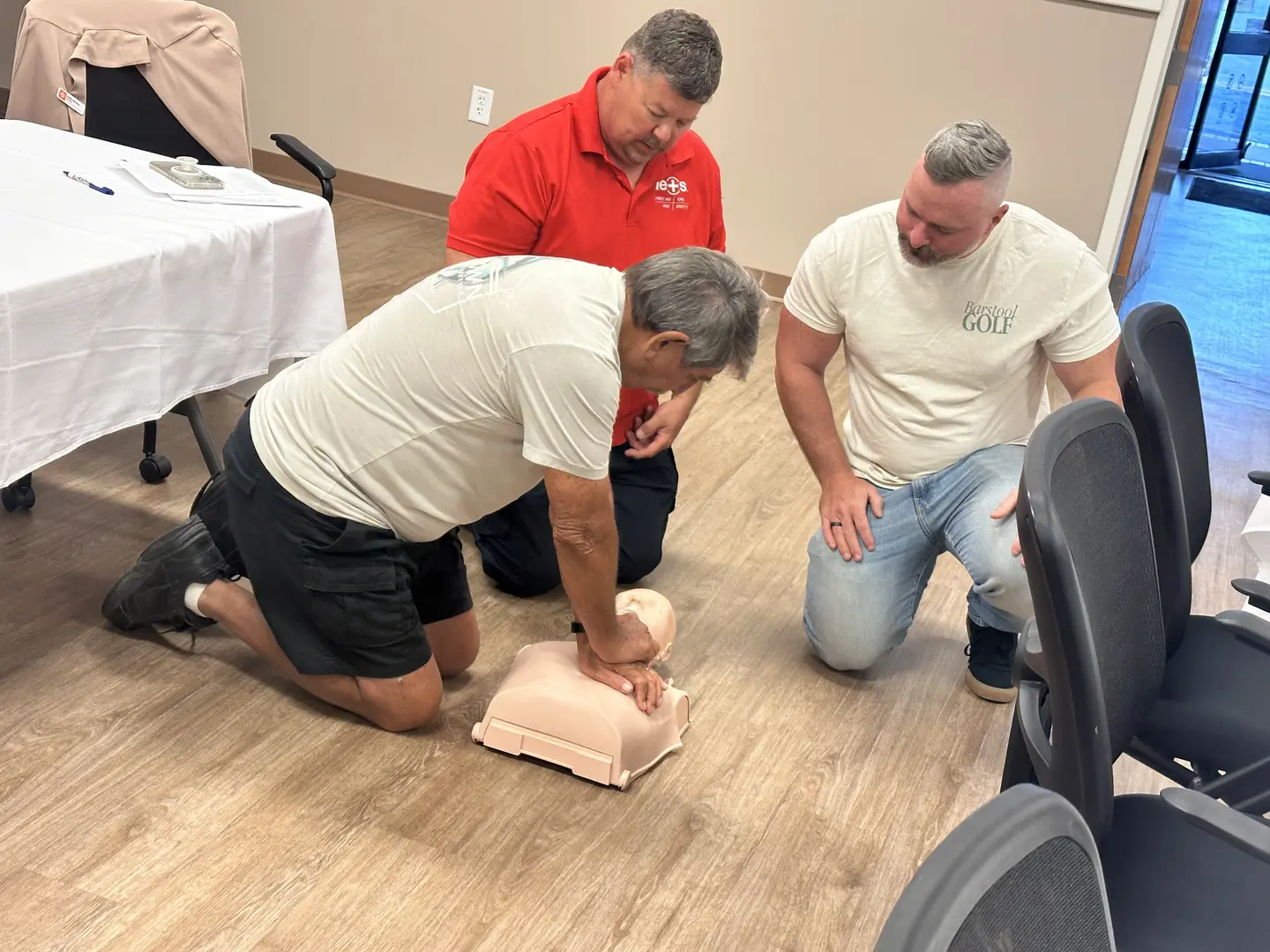 A coach practicing hands-only CPR on a training manikin as others look