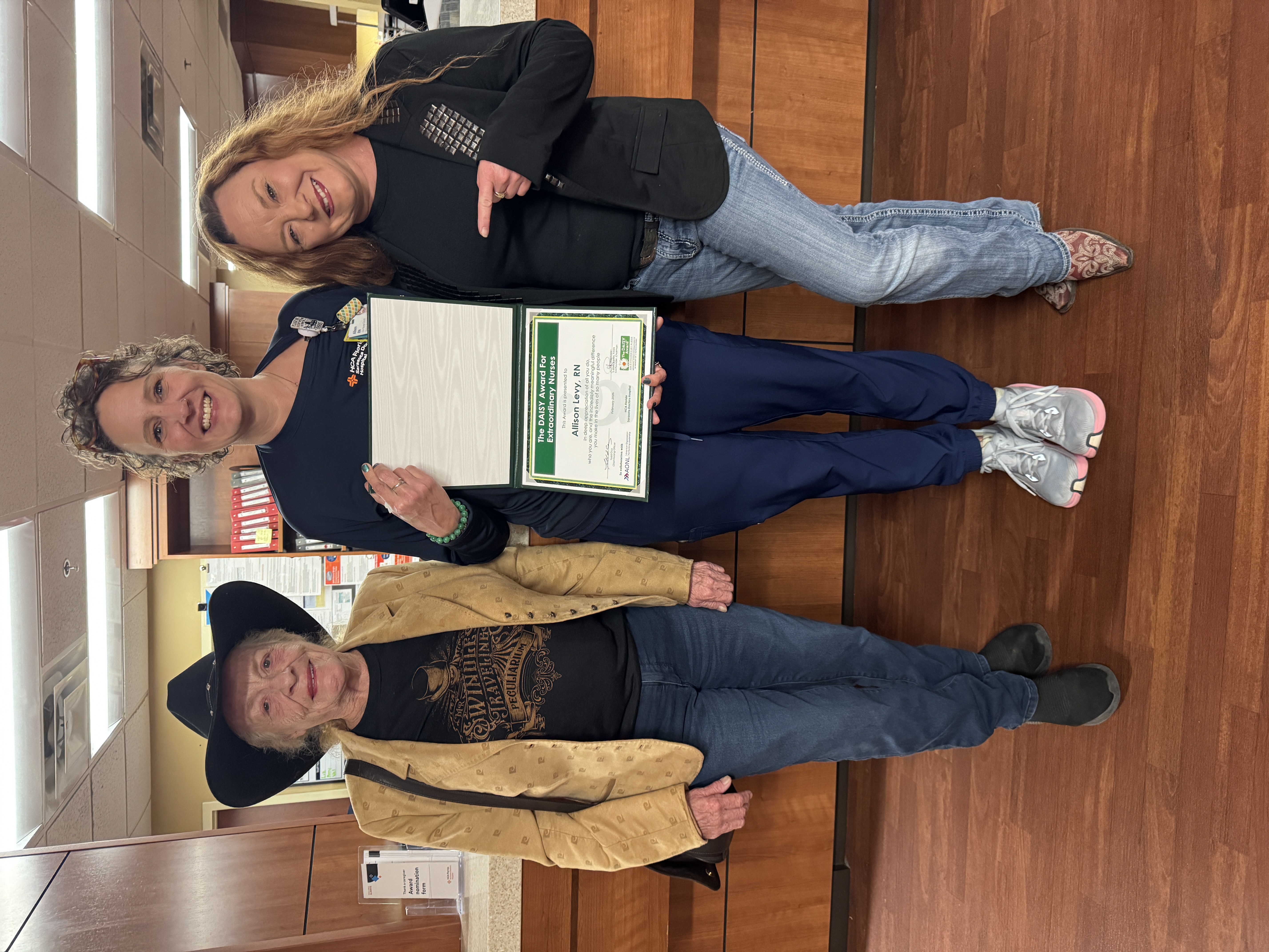 Nurse stands smiling and holding certificate with two people on each side of her.
