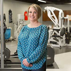 Michelle Hudson smiles while standing in a physical therapy exercise room.