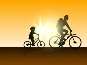 A man and a child riding their bikes with a sunburst behind them.
