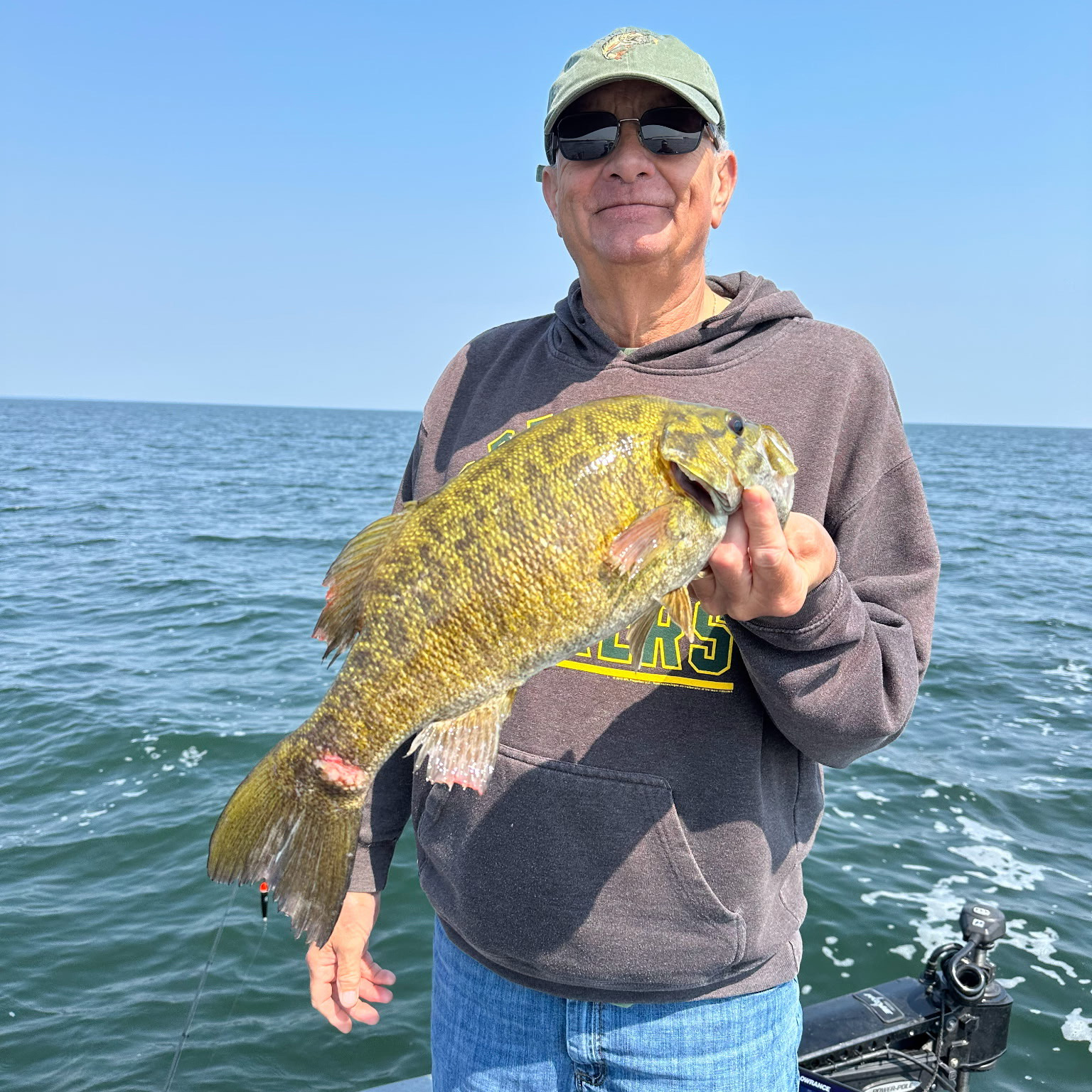 Patient Greg Stokes stands in a boat holding a fish and smiling.
