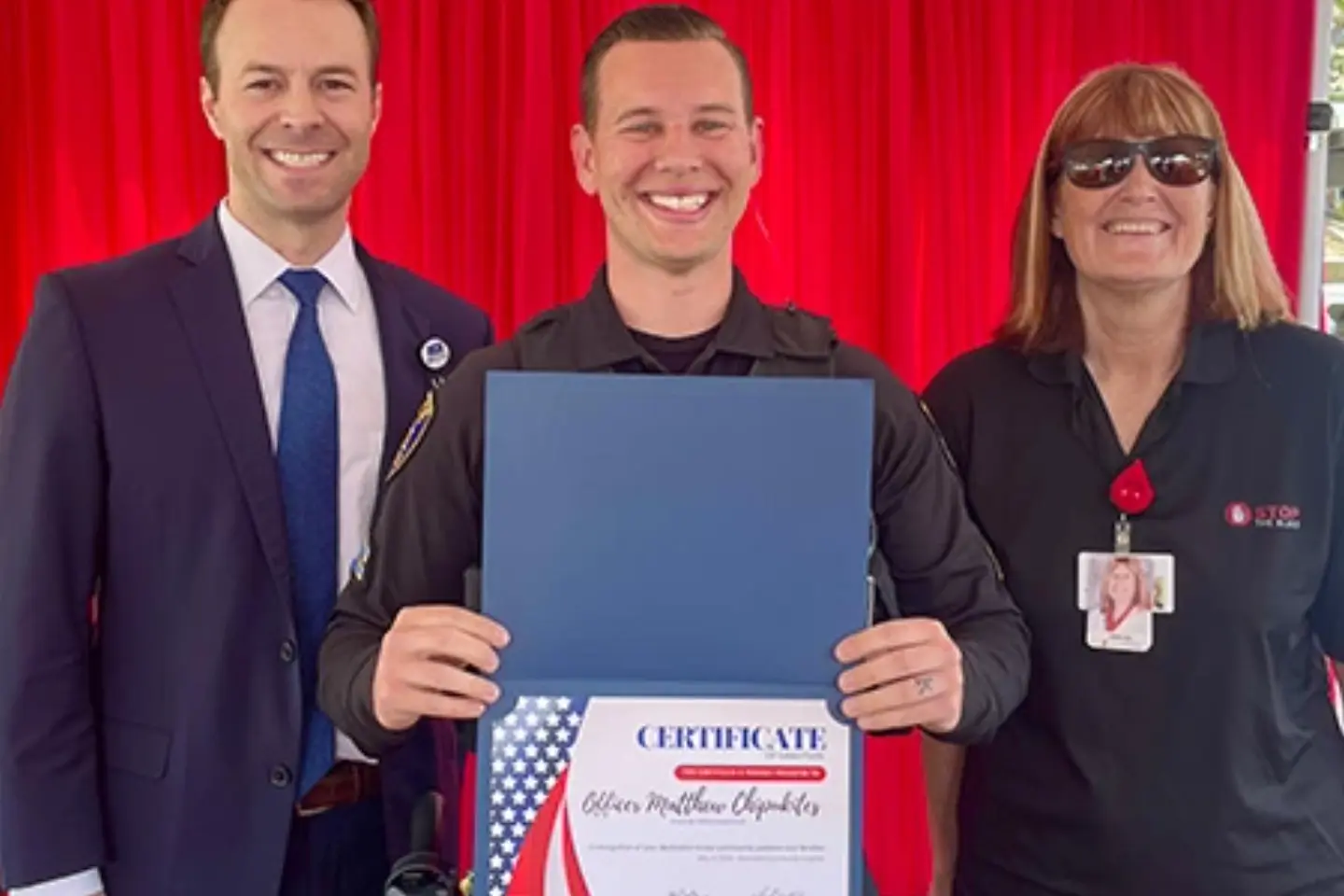 Police officer Matthew Chipukites smiles while holding a certificate recognizing him for  saving a life during a bleeding incident before EMS arrived.