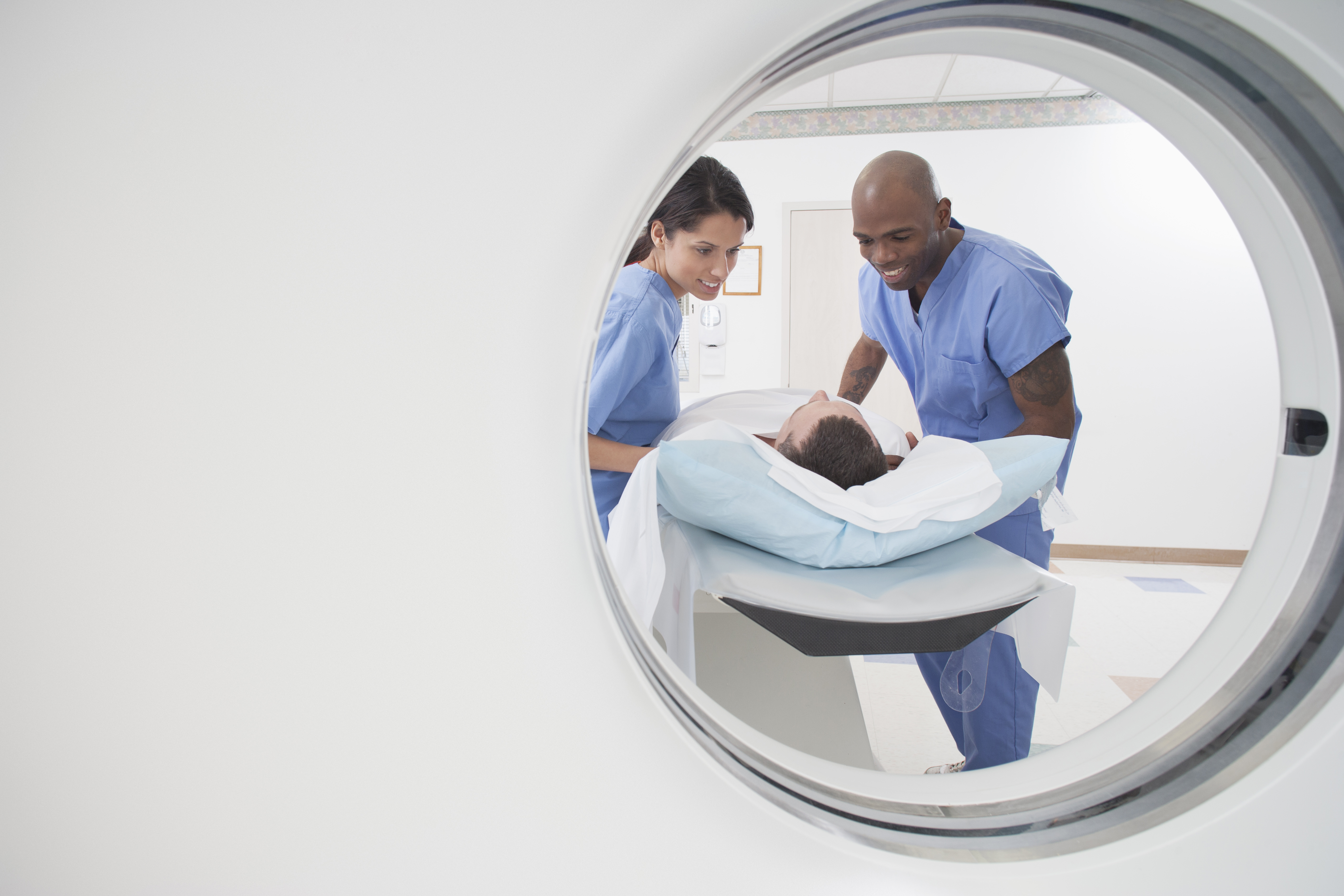 Nurses in scrubs speaking to a patient before he undergoes a CAT scan.