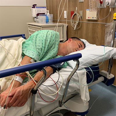 Colonoscopy patient Andy lies in a hospital bed on his side with a breathing tube visible on his face