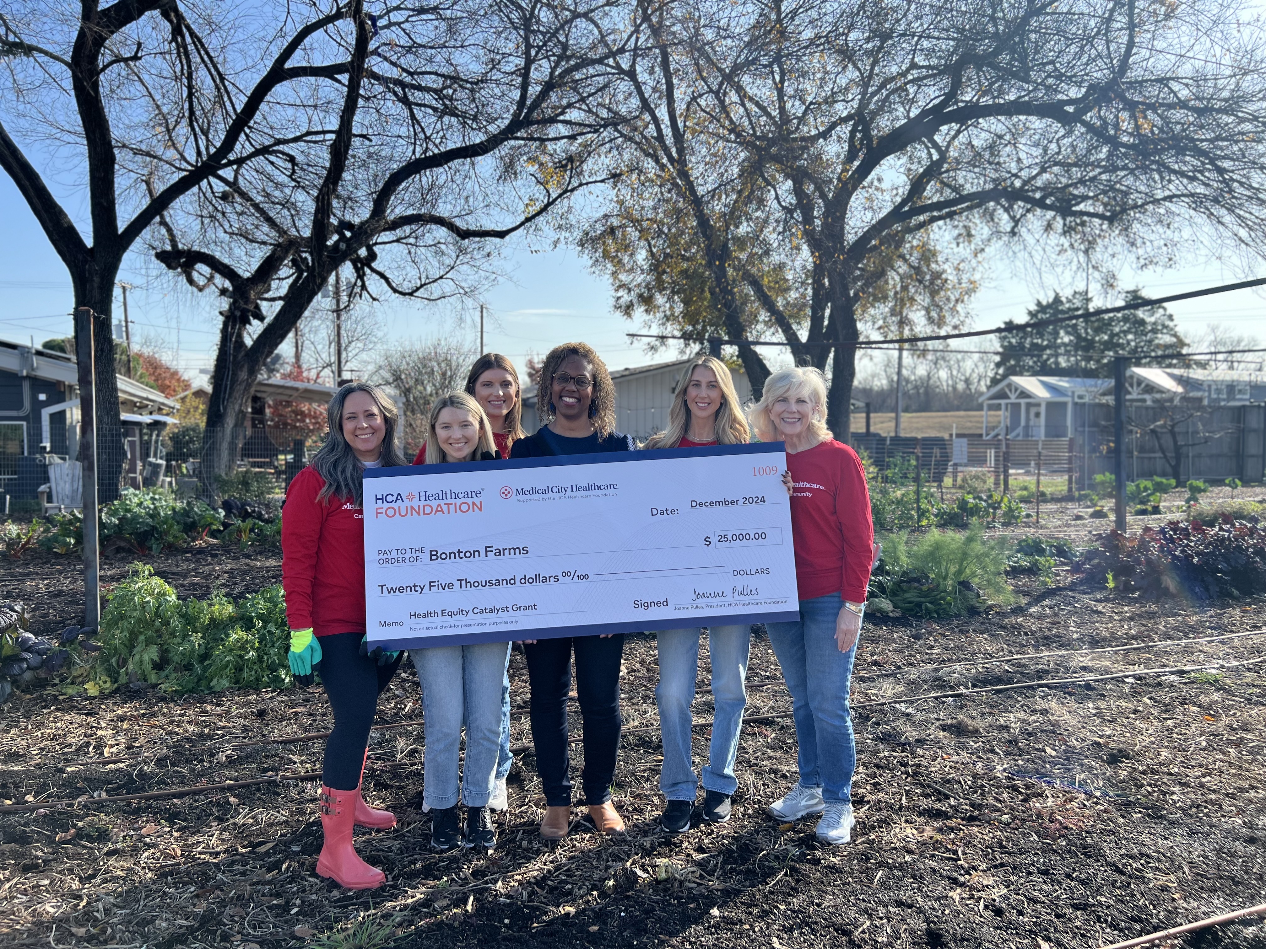 HCA Team on a farm holding a check to Bonton Farms