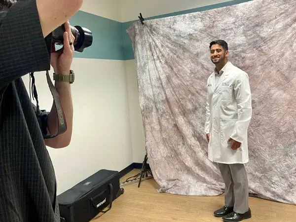 A smiling male medical resident poses for photo with photographer holding camera in studio.