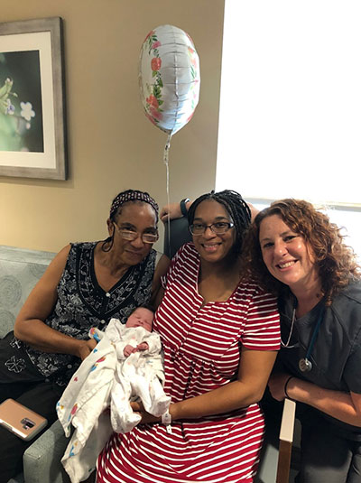 Nicole HP, surrounded by family and nurse, poses with newborn daughter.