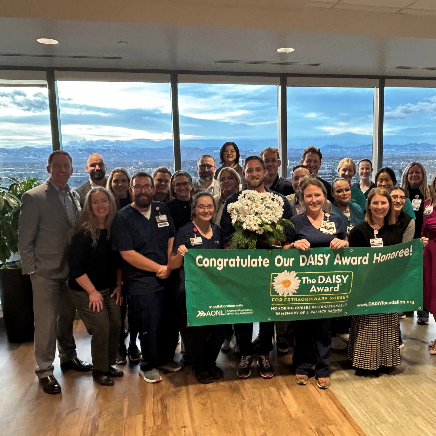 Jesse Ellis, RN and colleagues celebrate while holding the DAISY Awards banner.
