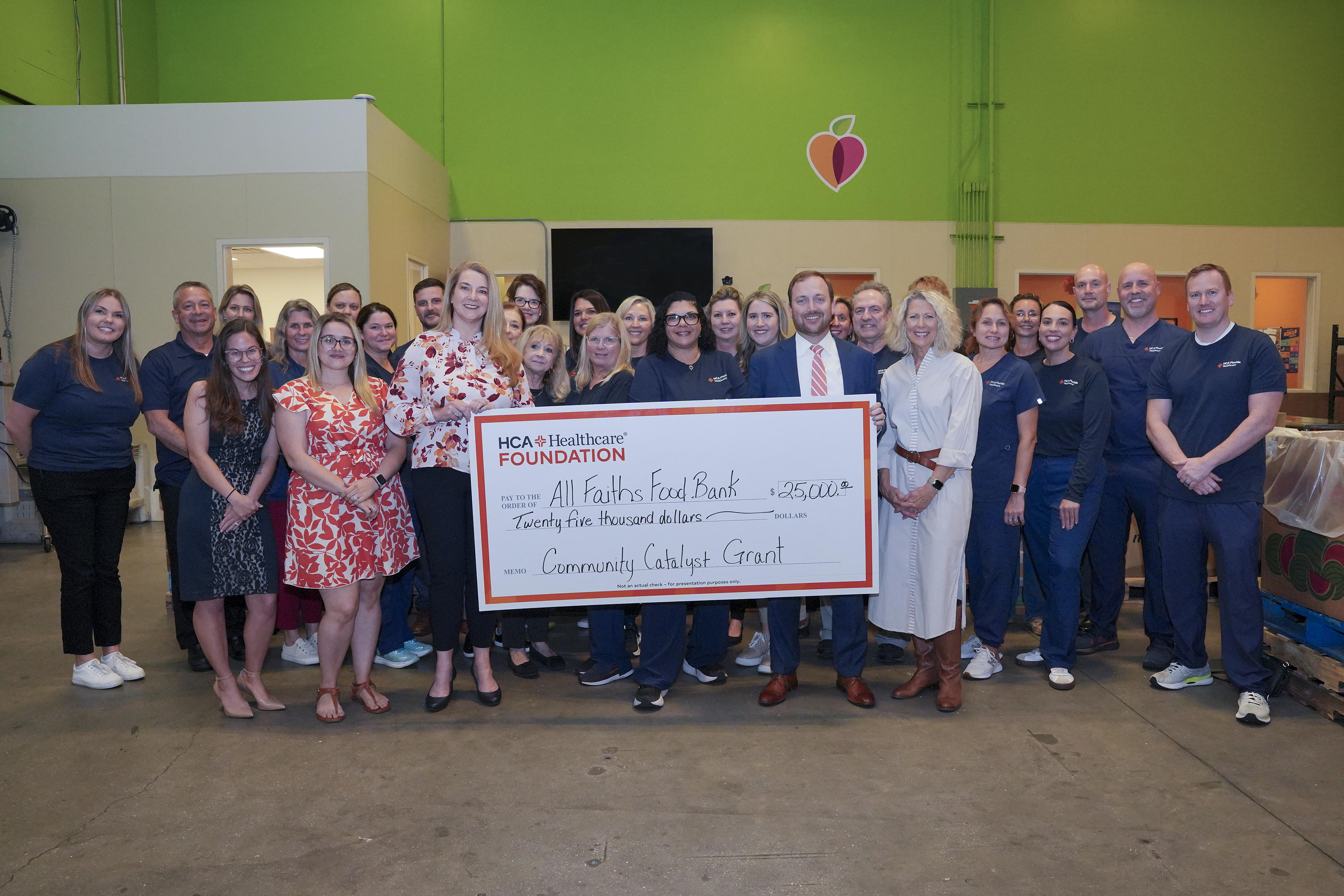 Large group of people stand smiling in a warehouse holding a large check.