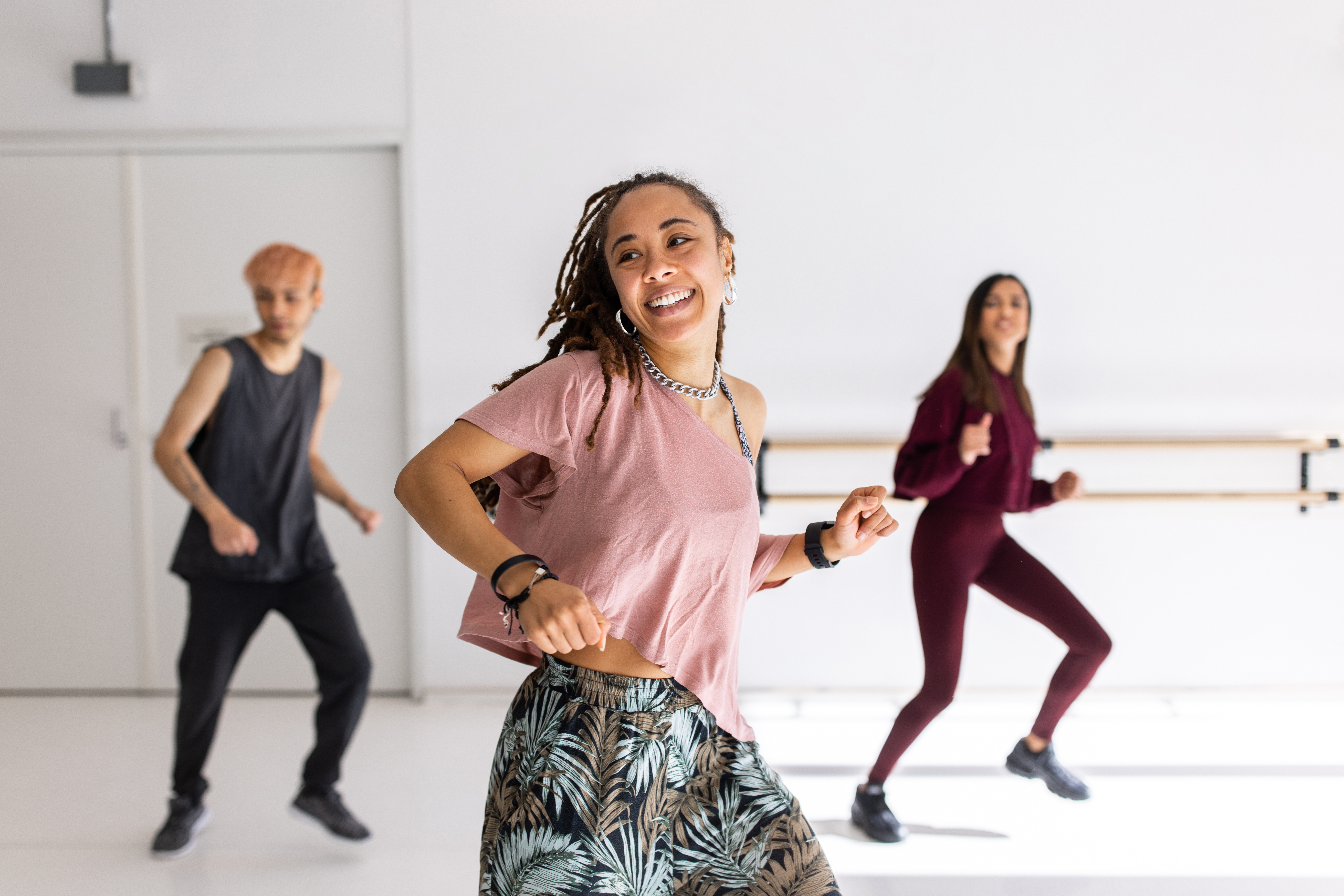A smiling young woman dancing in a fitness studio, with two others dancing behind her.