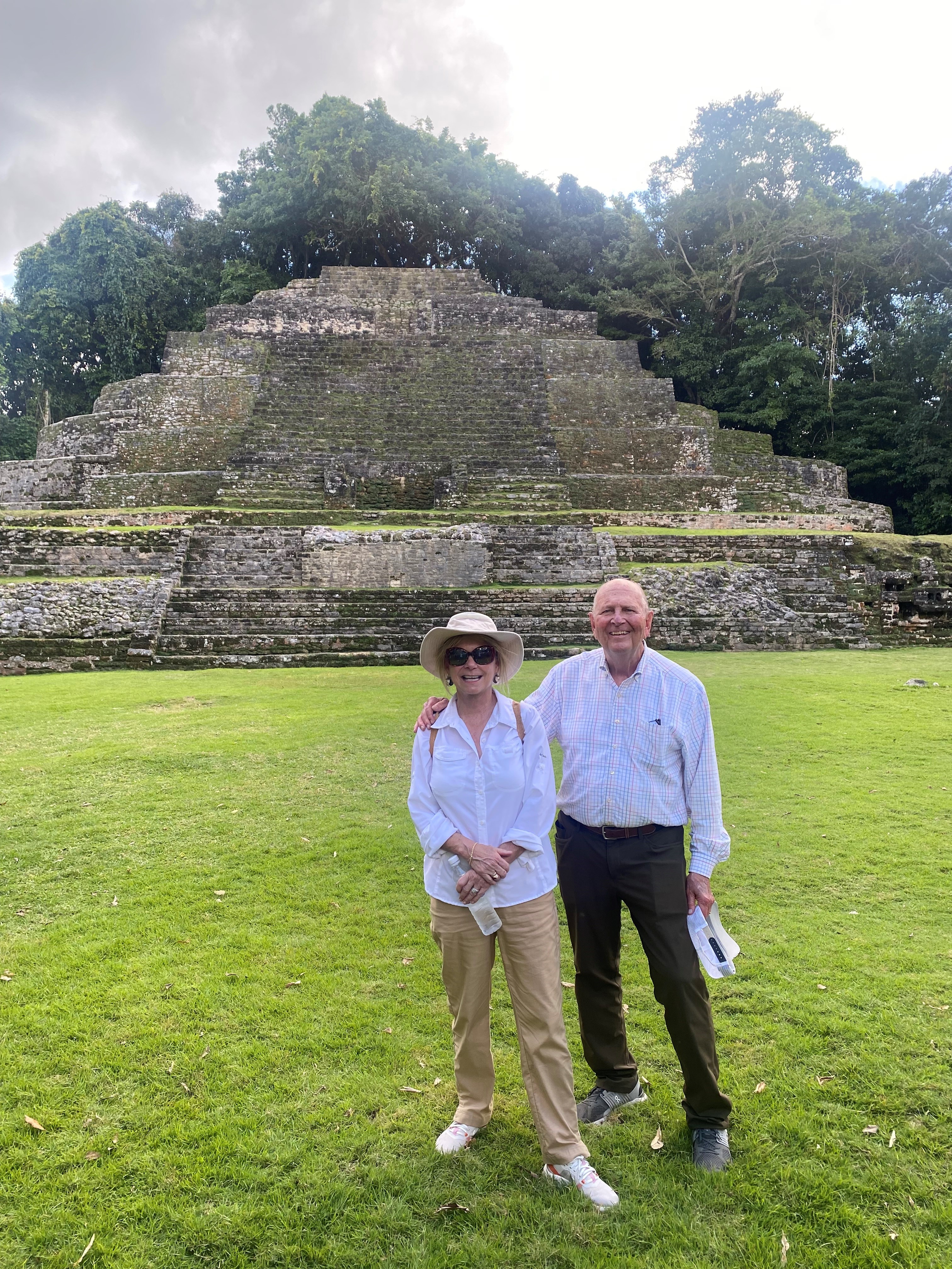 Couple smiling in front of a stone pyramid during their travels.