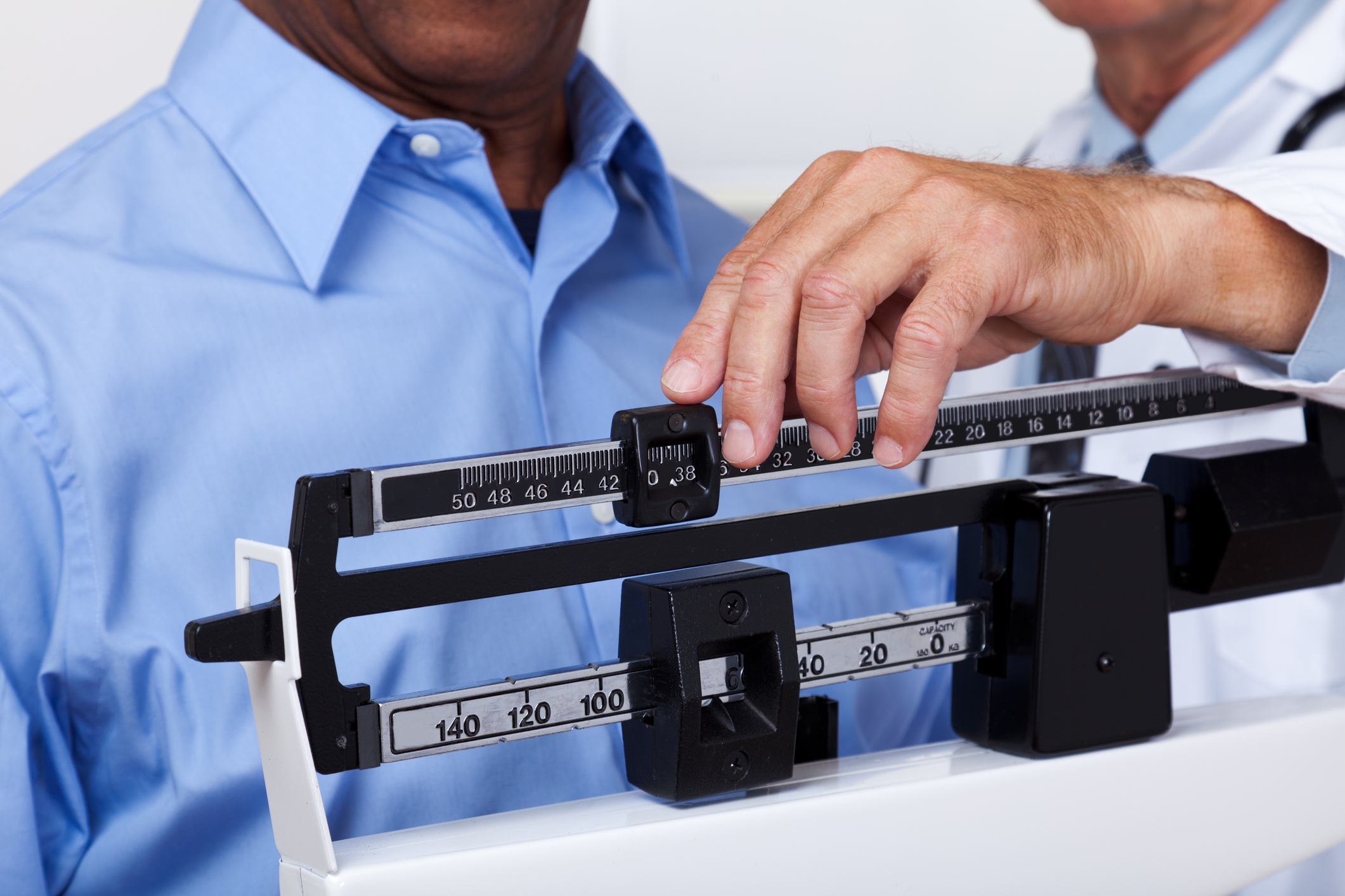 A patient stands on a mechanical scale, as a doctor adjusts it to check the patient's weight.