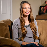 Abby is seated on a couch in a living room.