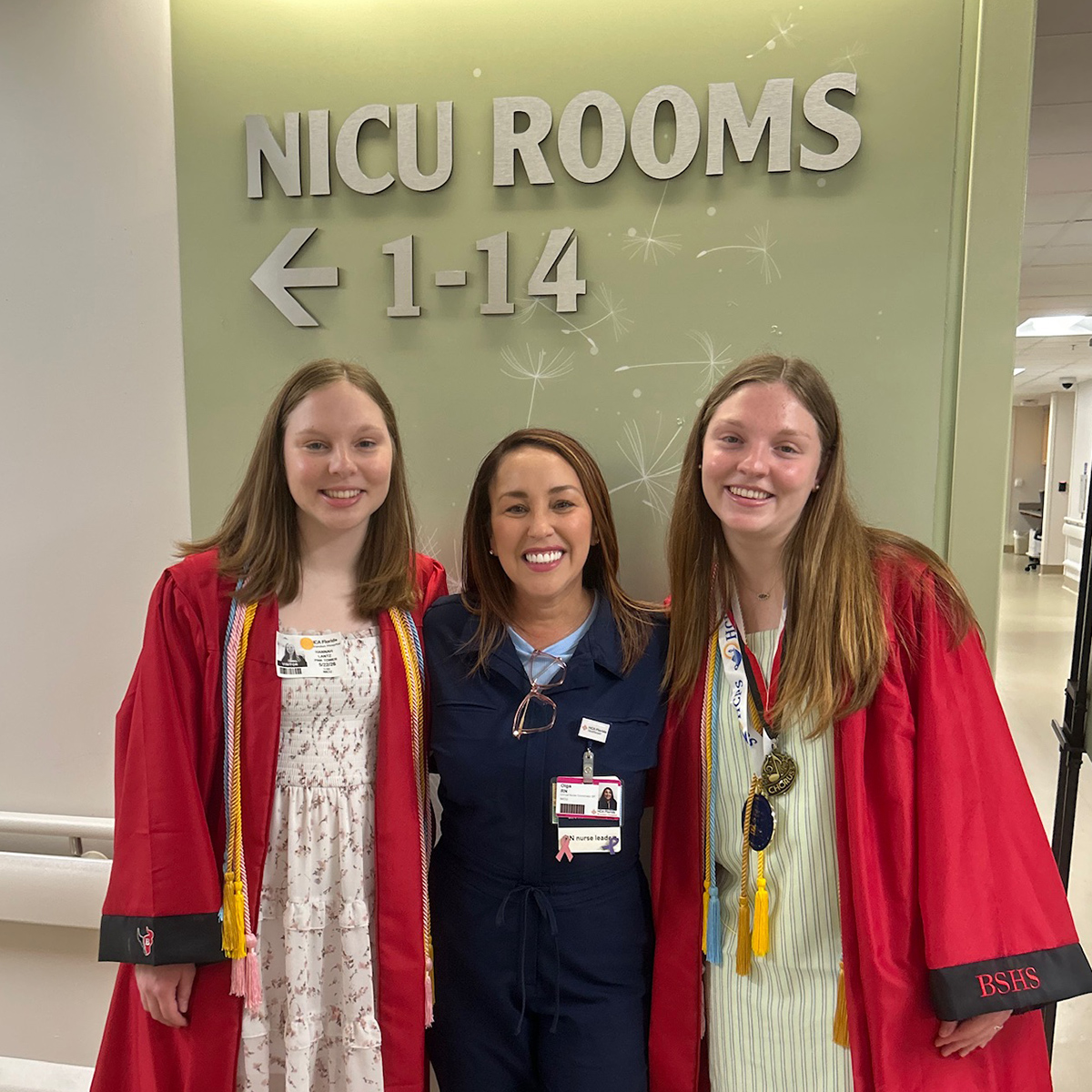Hannah and Kate in graduation gowns with NICU nurse in the hallway of Brandon Hospital NICU.