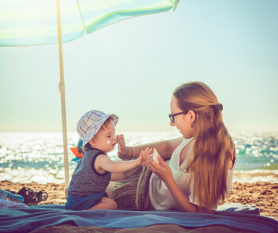 Mother applying sunscreen to child on a beach.