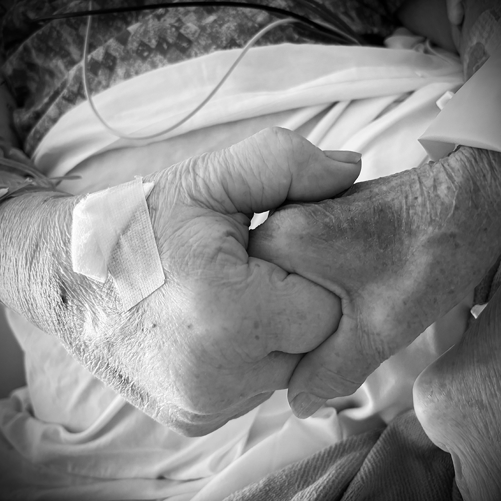 Joyce's hand being held by her husband's.