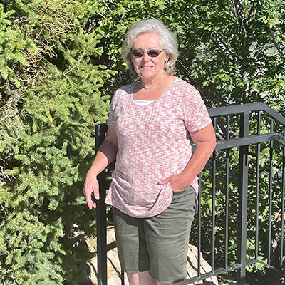 LeAnne Hunsaker poses by bushes and while leaning on a black railing in a sunny, outdoor setting