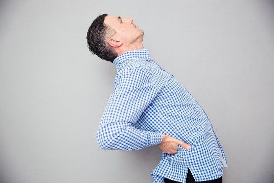 A man holds his lower back while bending backwards.