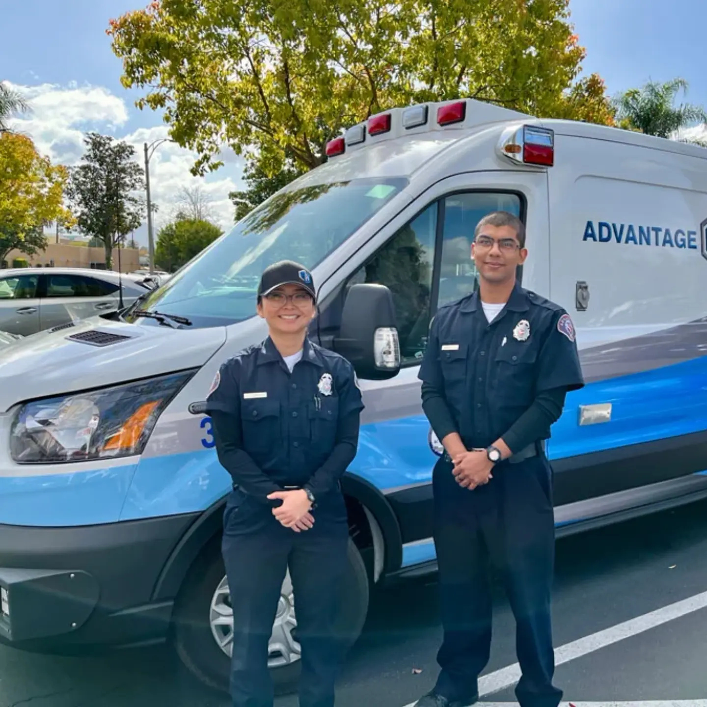 Two healthcare professionals smile while standing together in front of an Advantage Ambulance.