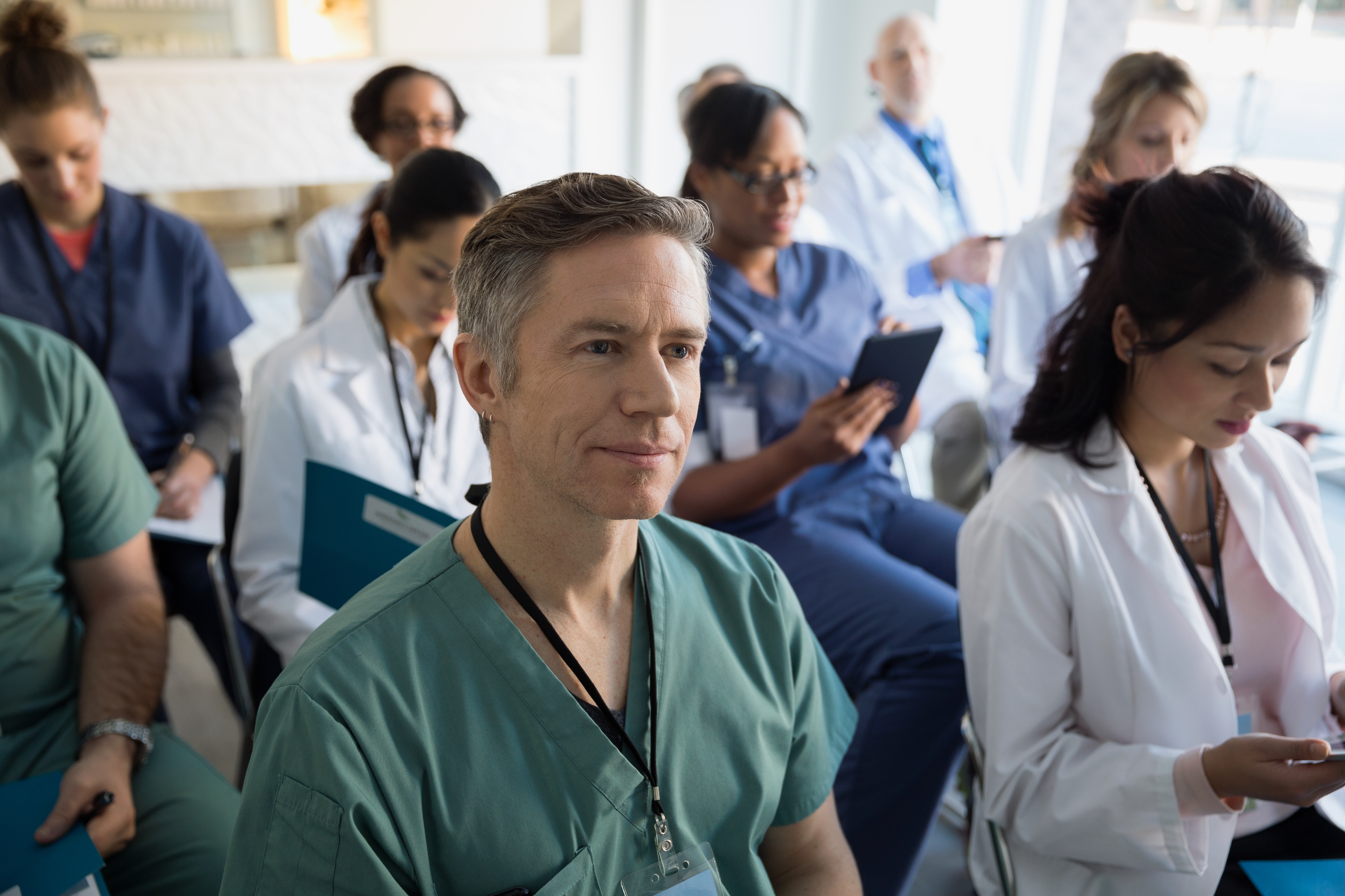 A group of physician residents sitting in rows in a room with medical coats/scrubs
