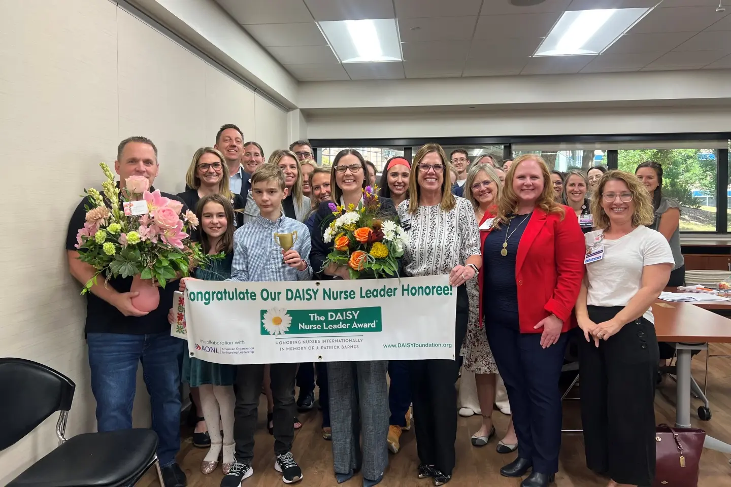 Rachel with large group of hospital team members pose with DAISY award banner.