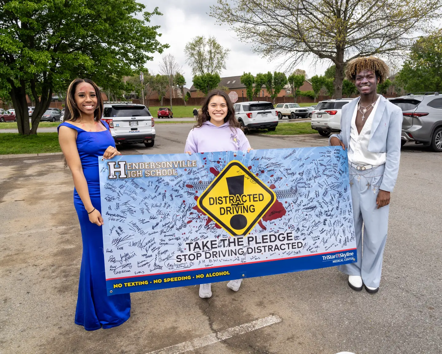 Three students who participated in the mock crash holding a pledge banner that students signed at the event.