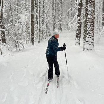 Carolyn cross-country skiing through a snowy forest.